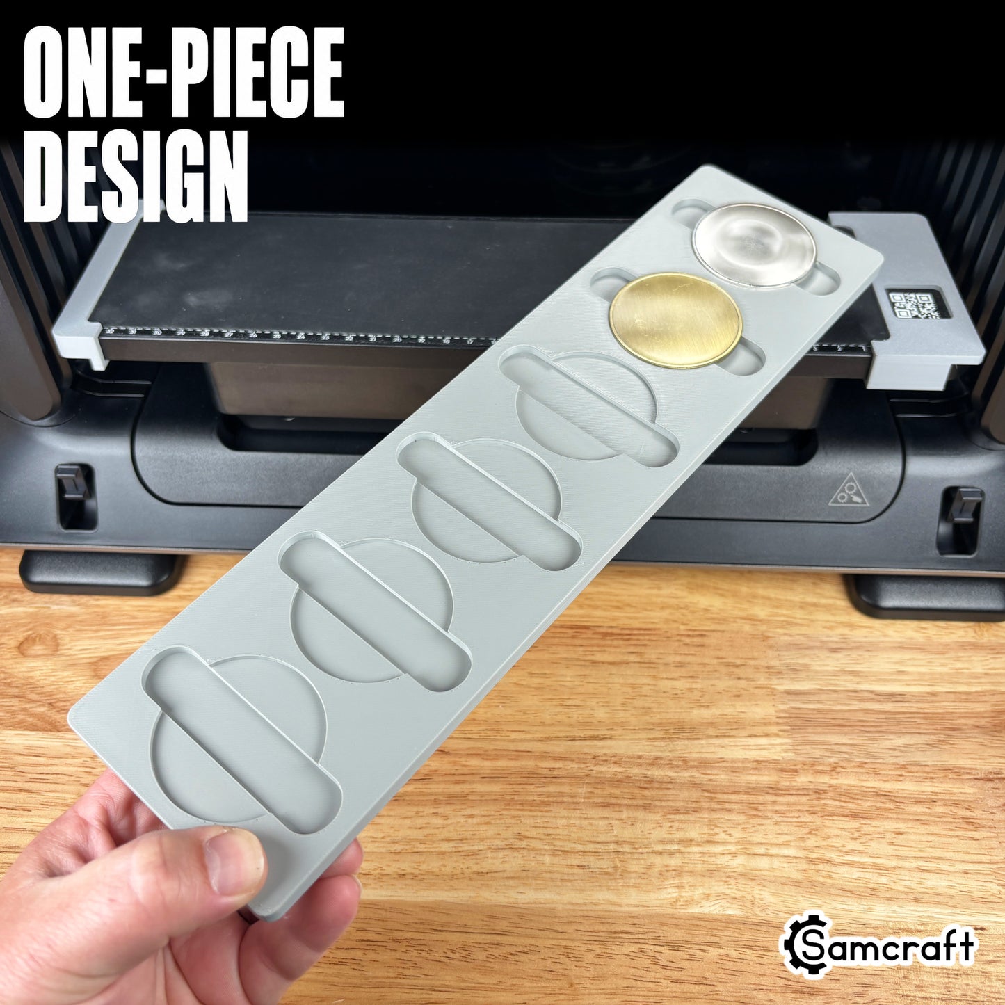 Hand holding the one-piece Samcraft Metal Coin Jig with gold and silver coin blanks in a gray 3D-printed tray with finger-relief cutouts on the eufyMake E1.