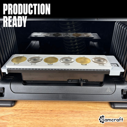 Production-ready Samcraft Metal Coin Jig holding a row of gold and silver metal coin blanks in recessed cradles on the eufyMake E1 UV printer bed.