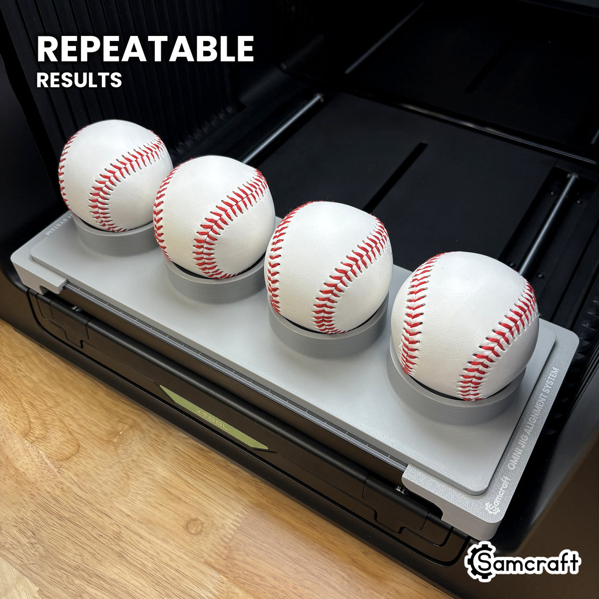 Angled view of the Samcraft baseball jig with four baseballs on the xTool Omni printer bed, for repeatable print placement.