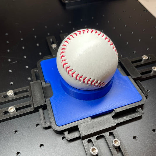 Samcraft blue sports ball jig on a ComMarker galvo laser bed, cradling a white baseball.