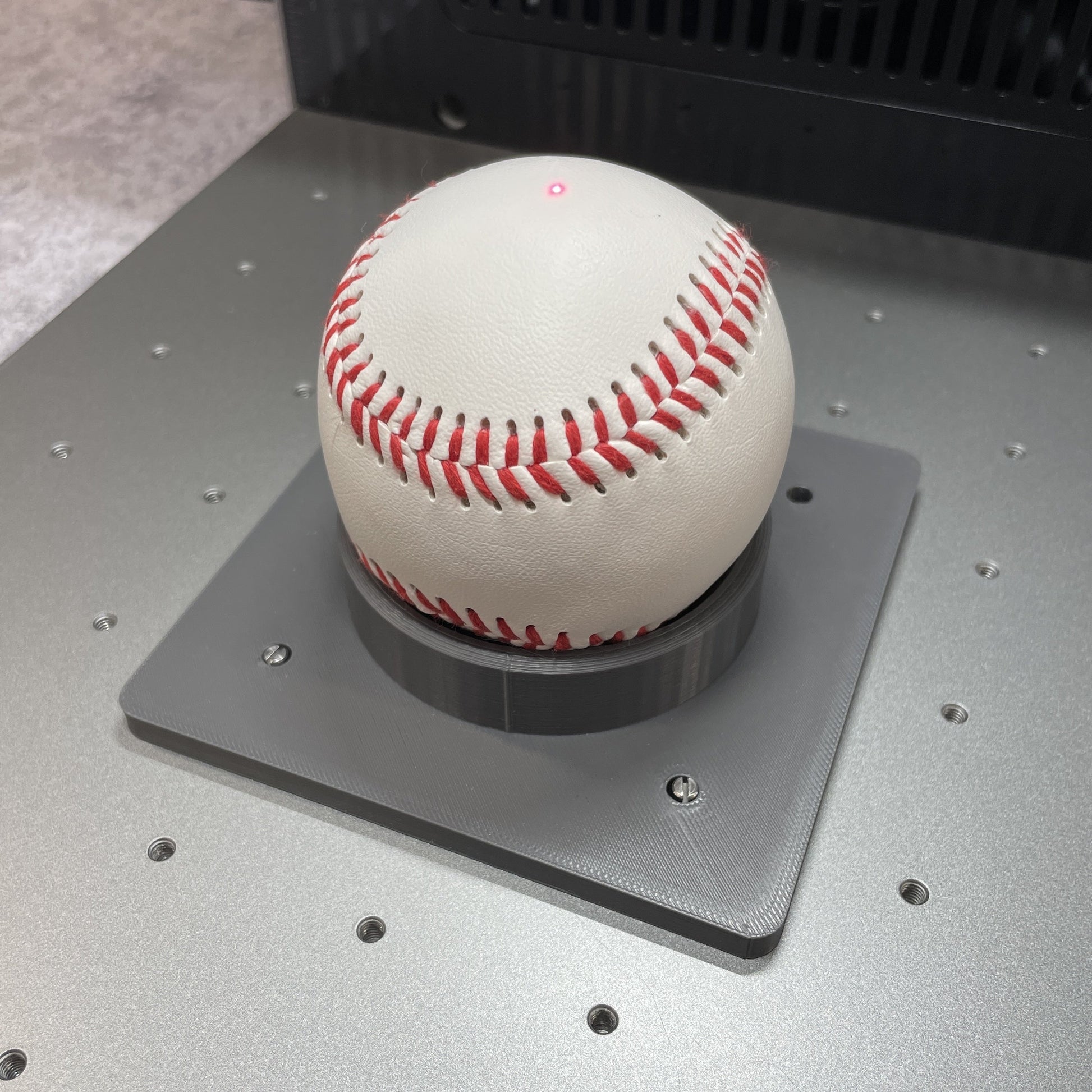 Samcraft sports ball jig on the xTool F2 Ultra bed, cradling a baseball in the centre recess.