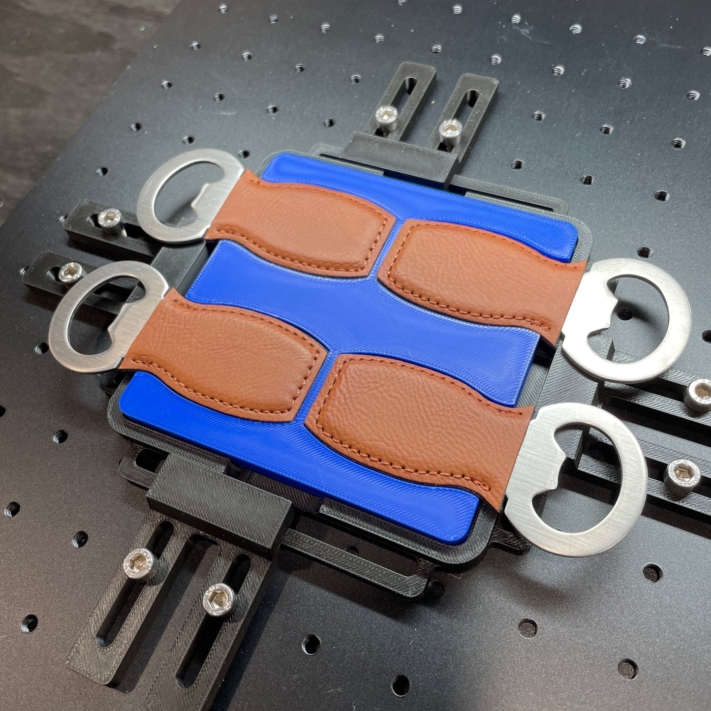 Samcraft blue small bottle opener jig on a ComMarker laser bed, holding four tan leather bottle openers with steel ends.
