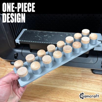 Hand holding the one-piece Samcraft Bottle Stopper Jig loaded with wood-topped bottle stoppers, showing tray strength on the eufyMake E1 UV printer.