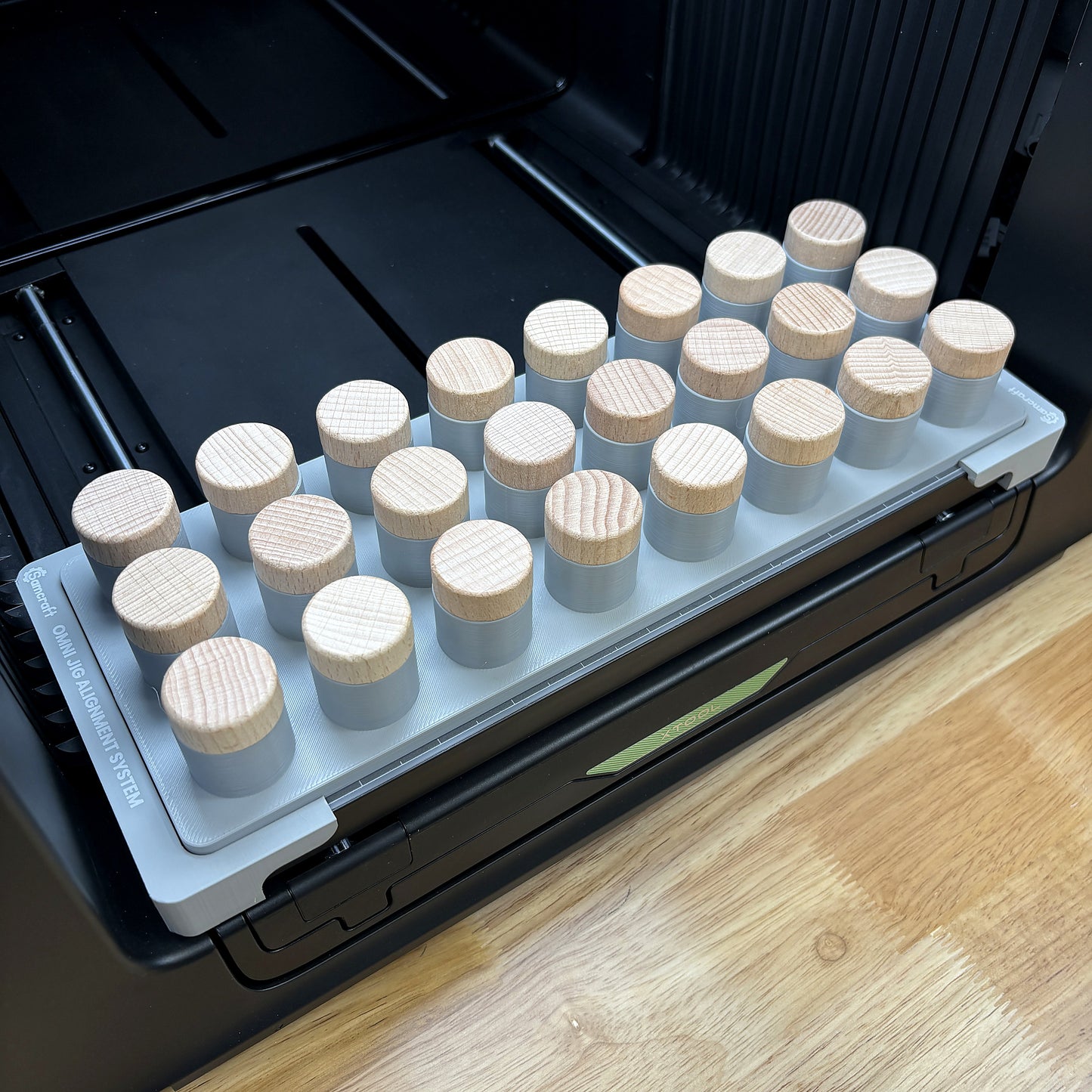 Samcraft bottle stopper jig on the bed of an xTool Omni UV printer, holding twenty-four wooden-top bottle stoppers upright.