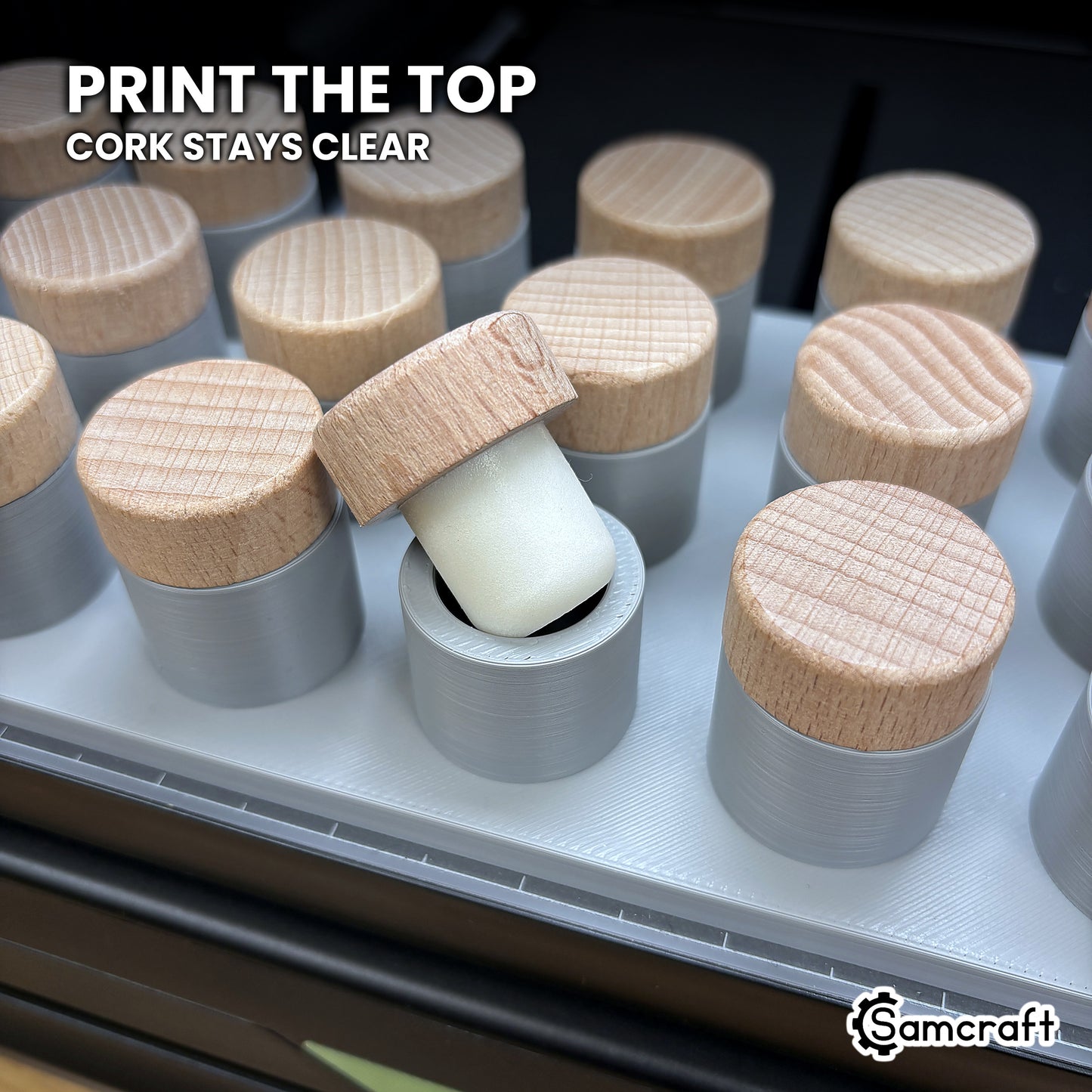A bottle stopper laid on its side beside seated stoppers in the Samcraft xTool Omni jig, showing the plug drops below the plate while the wooden top is printed.