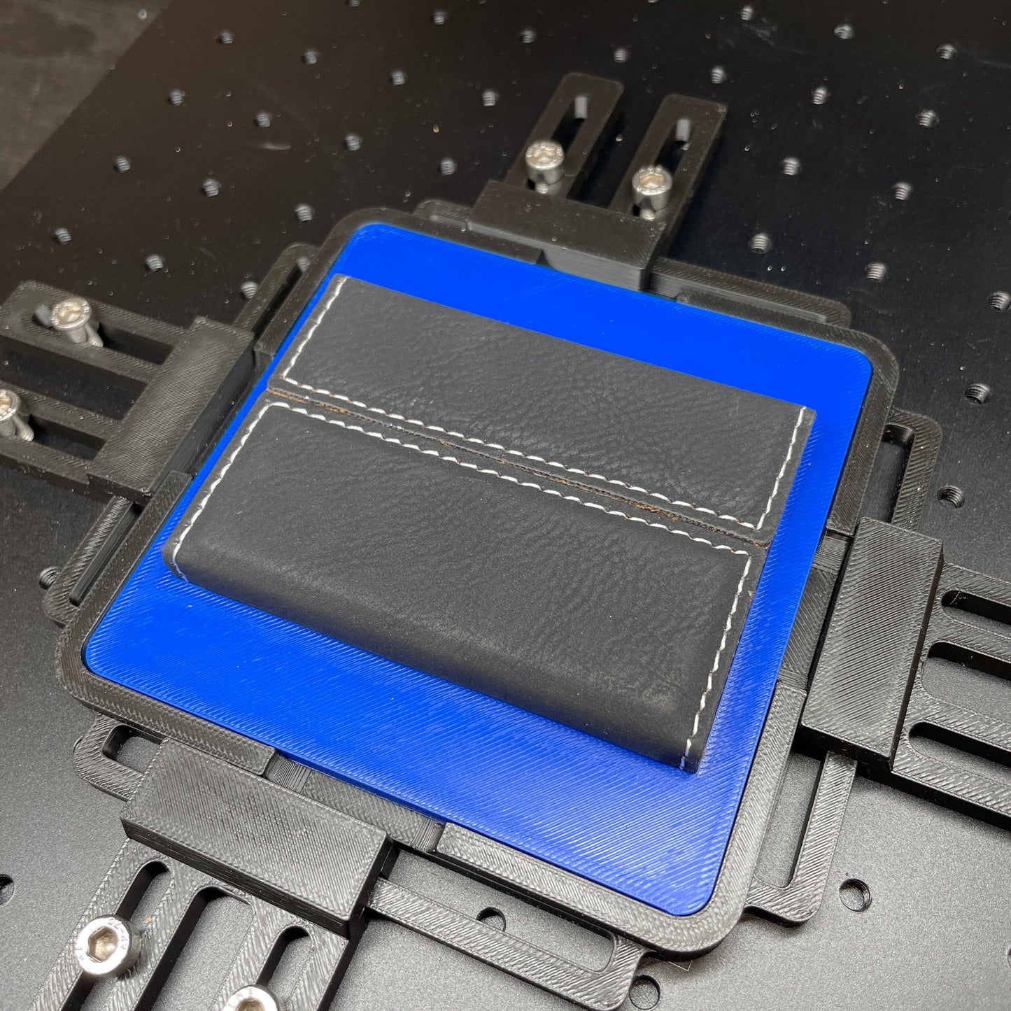 Samcraft blue business card case jig on a ComMarker laser bed, holding a black stitched leatherette card case.