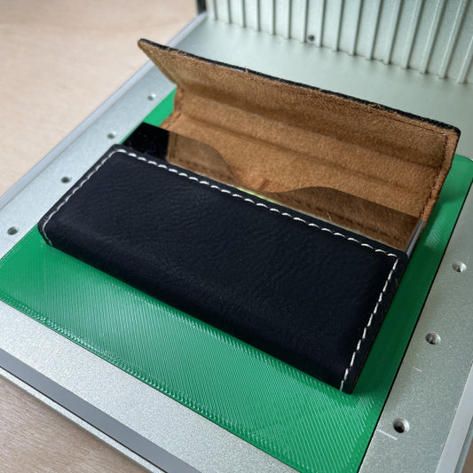 Samcraft business card case jig in an xTool F1 laser bed with a black leatherette card case open on it, showing the tan interior.