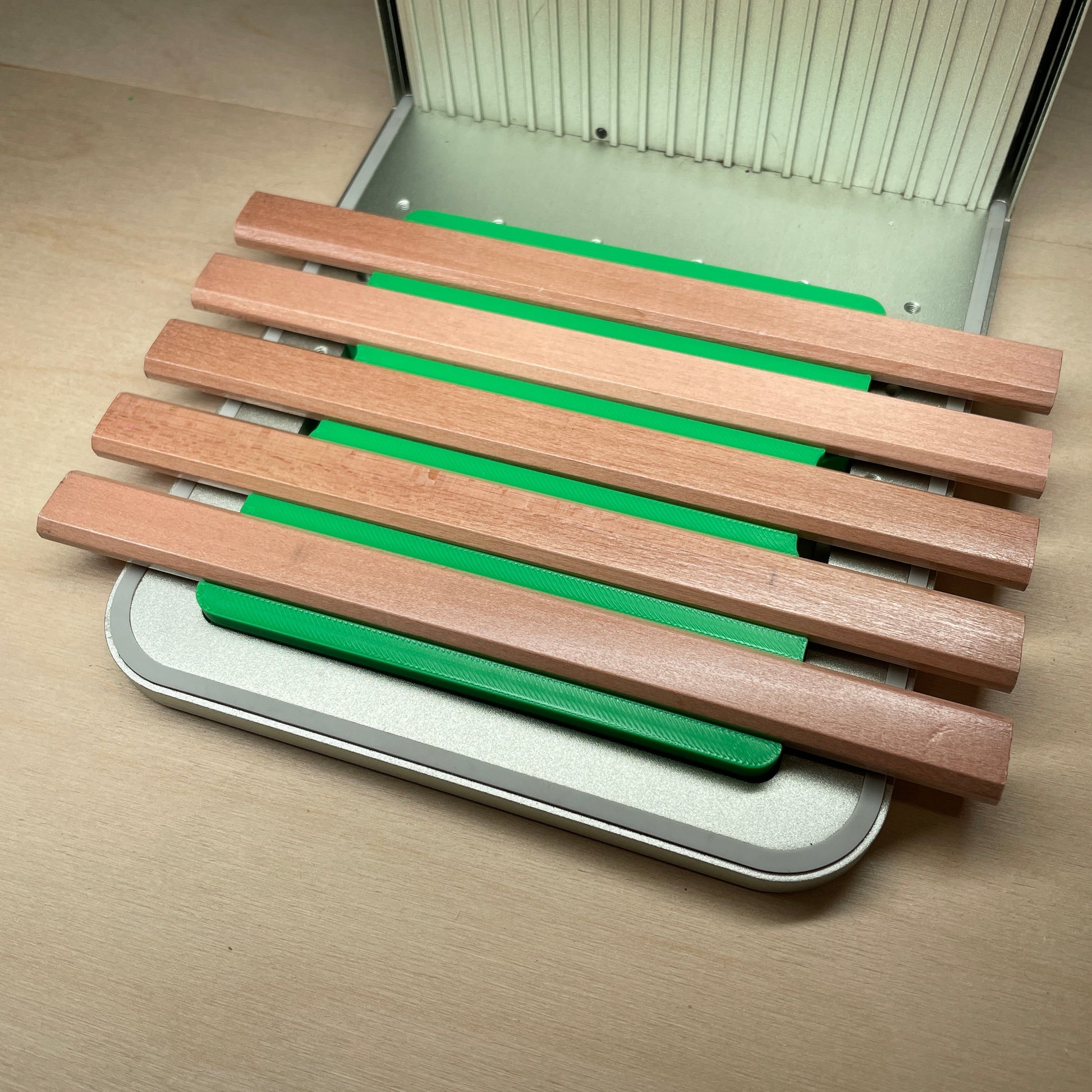 Samcraft green carpenter pencil jig in an xTool F1 laser bed, holding a row of flat wooden carpenter pencils.