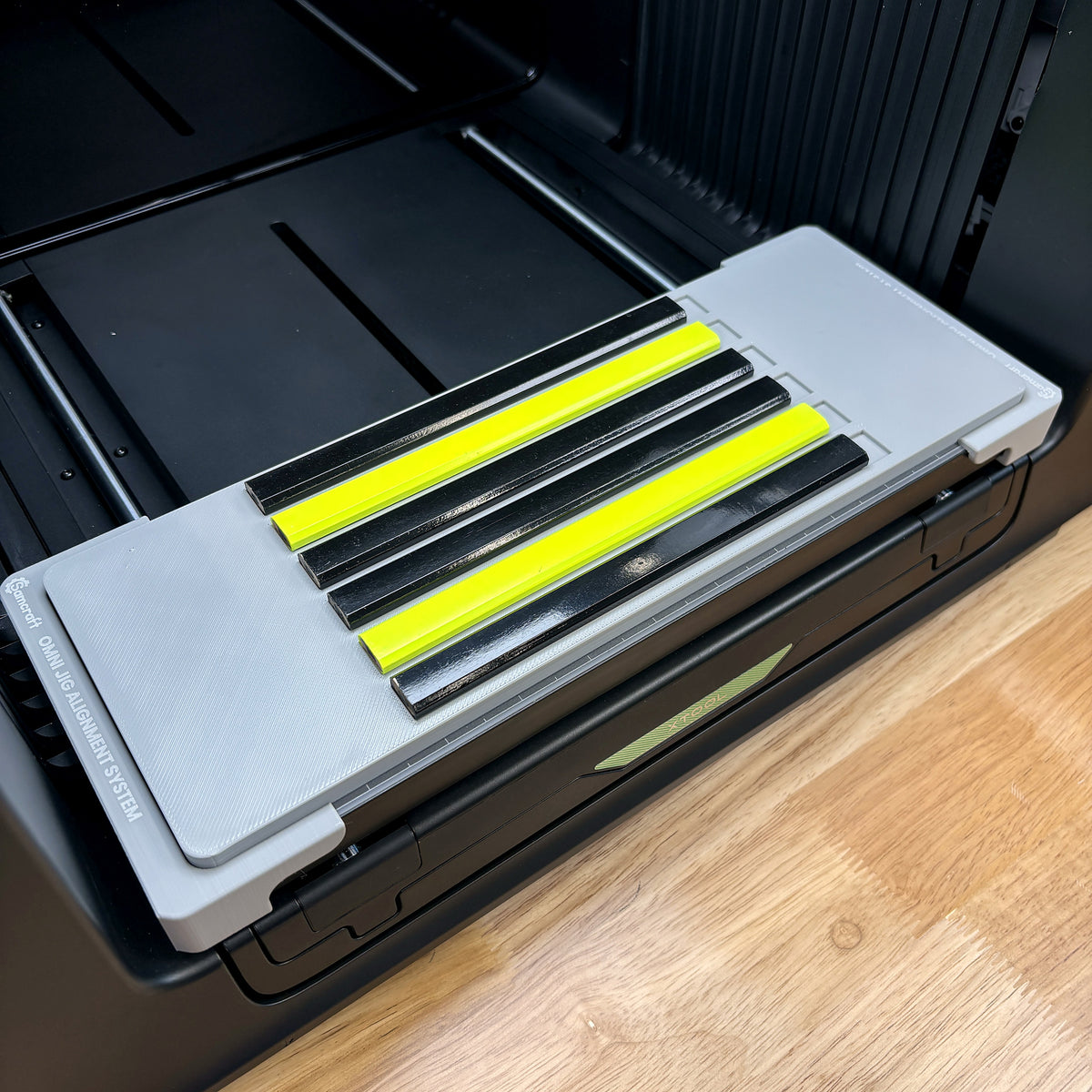 Samcraft carpenter pencil jig seated on the Omni Jig Alignment System inside an xTool Omni UV printer, holding six black and neon yellow carpenter pencils.