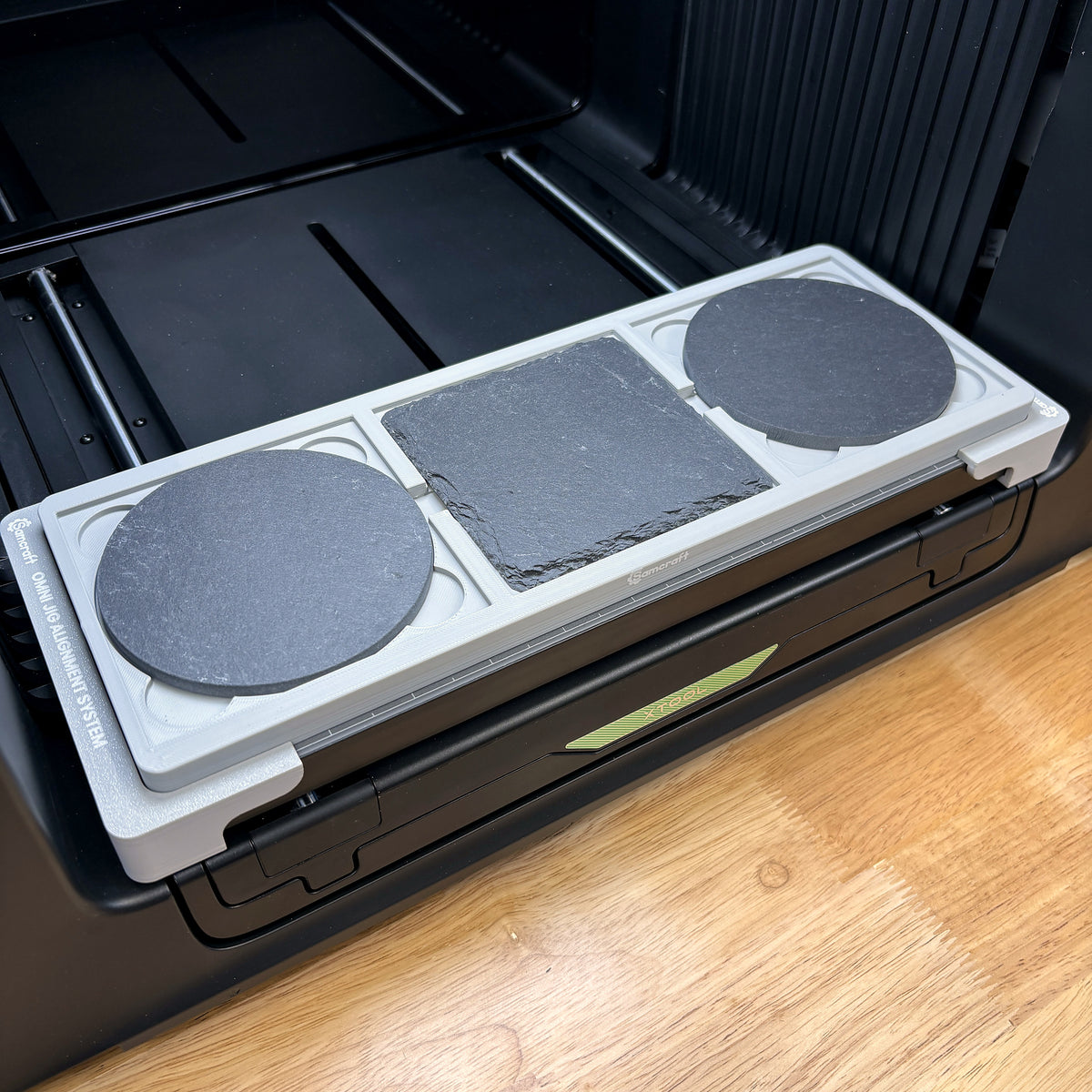 Samcraft 4 inch drink coaster jig on the bed of an xTool Omni UV printer, holding two round slate coasters and one square.