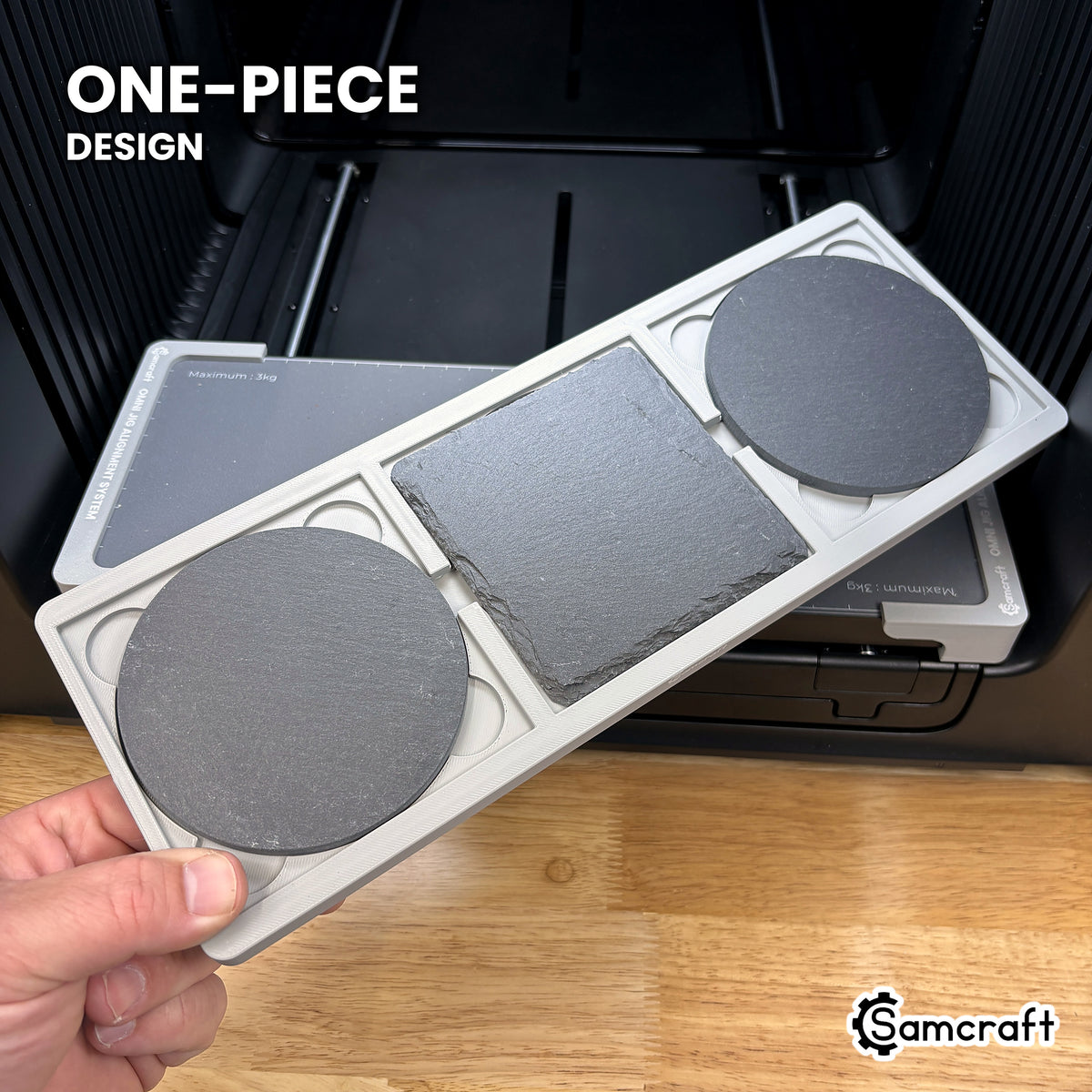 Hand holding the one-piece Samcraft 4 inch drink coaster jig for the xTool Omni, three slate coasters seated in a single molded tray.