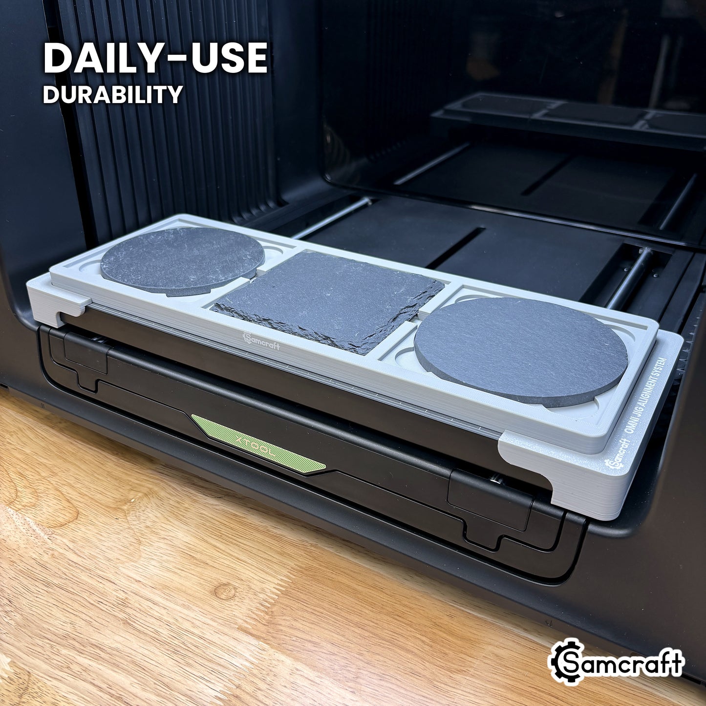 Samcraft coaster jig in high-temperature rated plastic holding three slate coasters on the xTool Omni bed, built for daily-use durability.