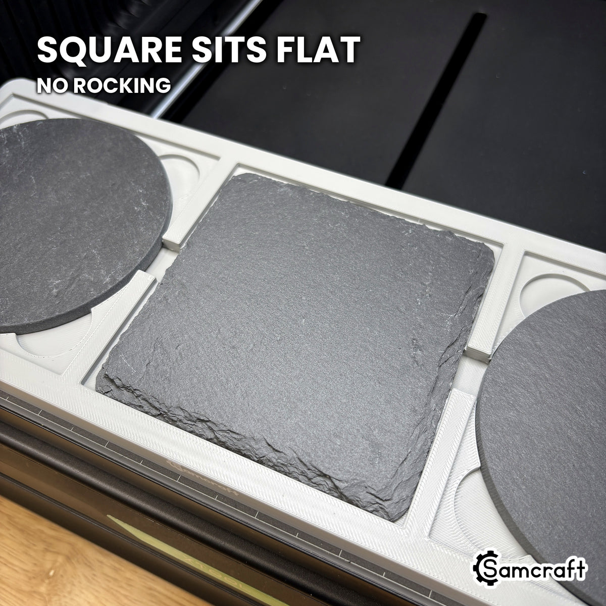 Square slate coaster seated flat in the Samcraft xTool Omni coaster jig, with recesses for the coaster's feet so it does not rock.