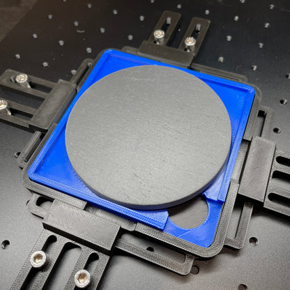 Samcraft blue 4 inch drink coaster jig on a ComMarker laser bed, holding a round grey slate coaster.