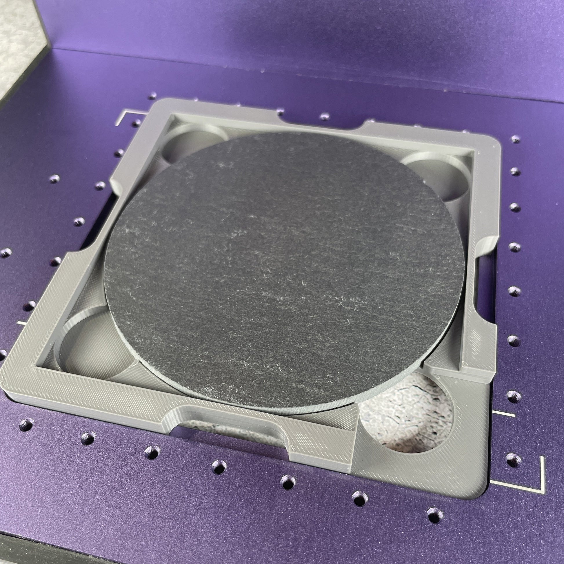 Samcraft 4 inch drink coaster jig on the purple bed of a WeCreat Lumos, holding a round slate coaster.