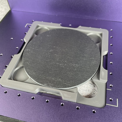 Samcraft 4 inch drink coaster jig on the purple bed of a WeCreat Lumos, holding a round slate coaster.