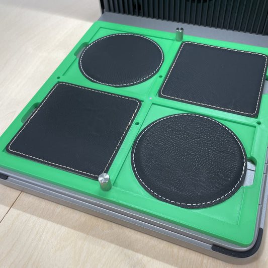 Samcraft green 99mm drink coaster jig in an xTool F1 Ultra laser bed, holding round and square black leatherette coasters.