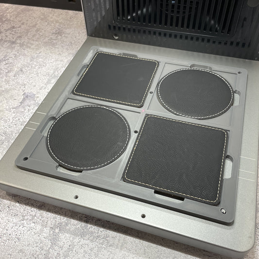 Samcraft 99mm drink coaster jig on the xTool F2 Ultra bed, holding round and square dark leatherette coasters.