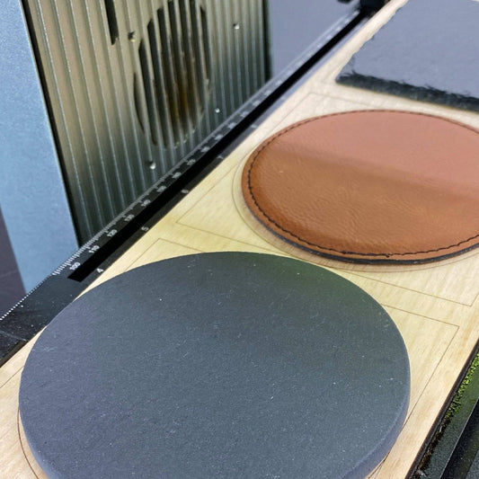 Samcraft drink coaster template on the xTool F1 slide extension, holding a black slate coaster and a brown leatherette coaster.