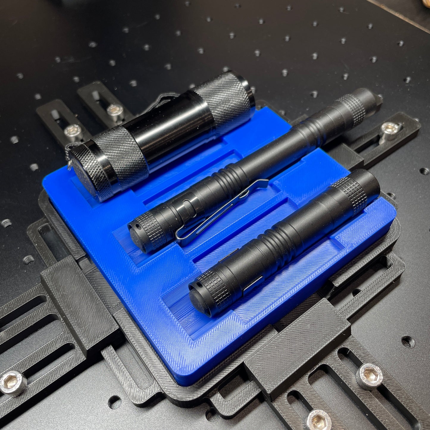 Samcraft blue flashlight jig on a ComMarker laser bed, holding three black aluminium flashlights.