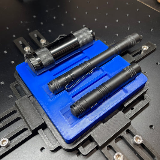 Samcraft blue flashlight jig on a ComMarker laser bed, holding three black aluminium flashlights.