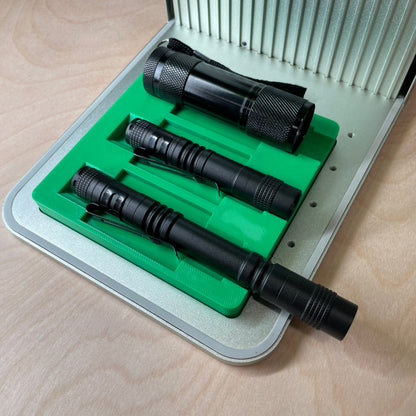 Samcraft green flashlight jig in an xTool F1 laser bed, holding three black flashlights of different lengths in stepped channels.