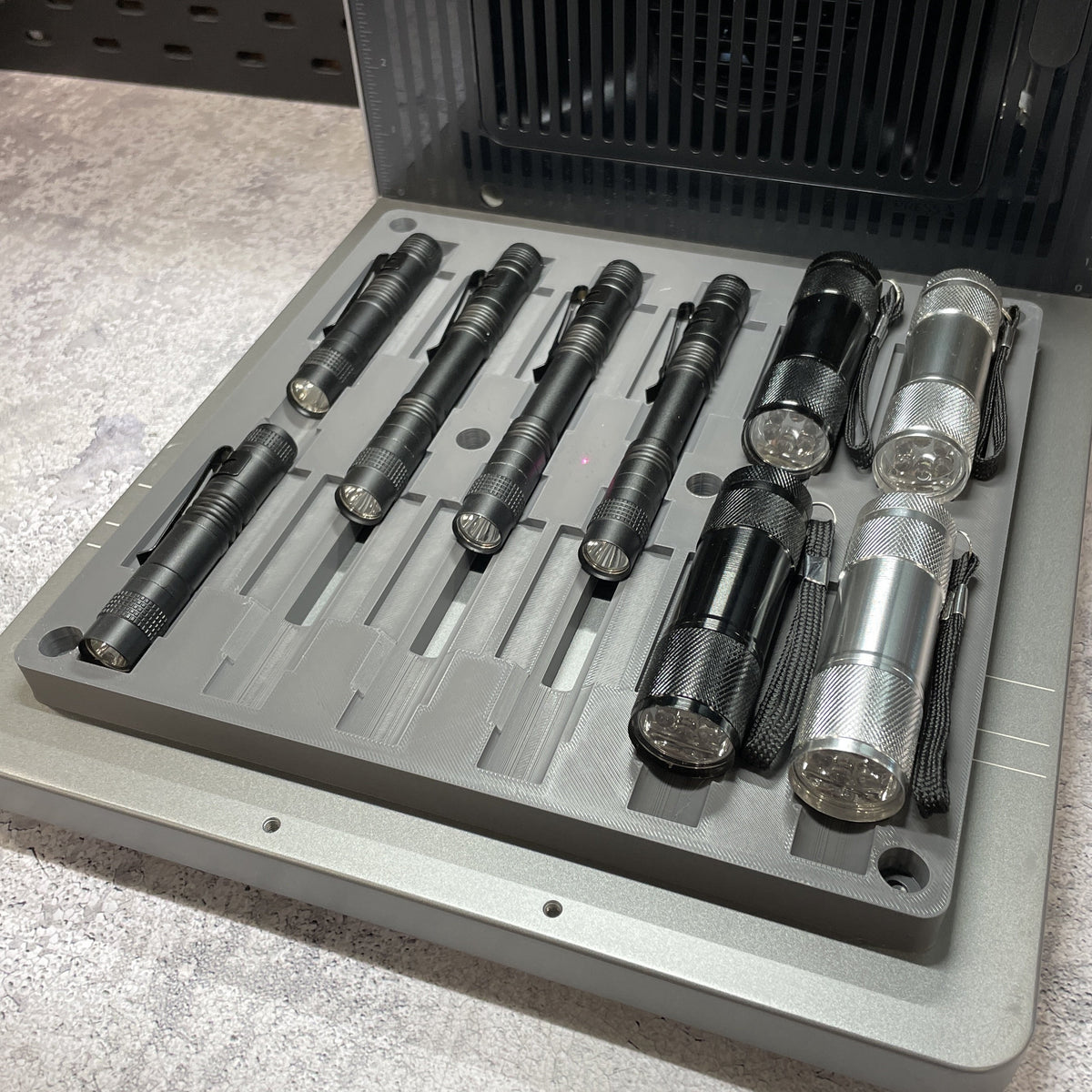 Samcraft flashlight jig on the xTool F2 Ultra bed, holding several black and stainless flashlights in stepped channels.
