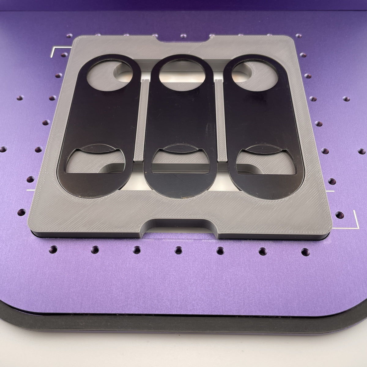 Samcraft flat metal keychain bottle opener jig on the purple bed of a WeCreat Lumos, holding three black oval bottle openers.