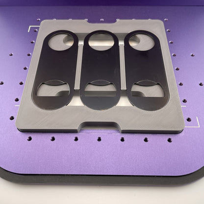 Samcraft flat metal keychain bottle opener jig on the purple bed of a WeCreat Lumos, holding three black oval bottle openers.