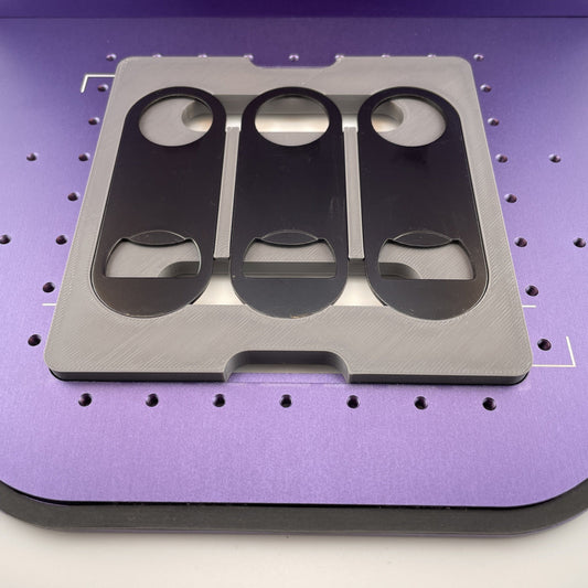 Samcraft flat metal keychain bottle opener jig on the purple bed of a WeCreat Lumos, holding three black oval bottle openers.