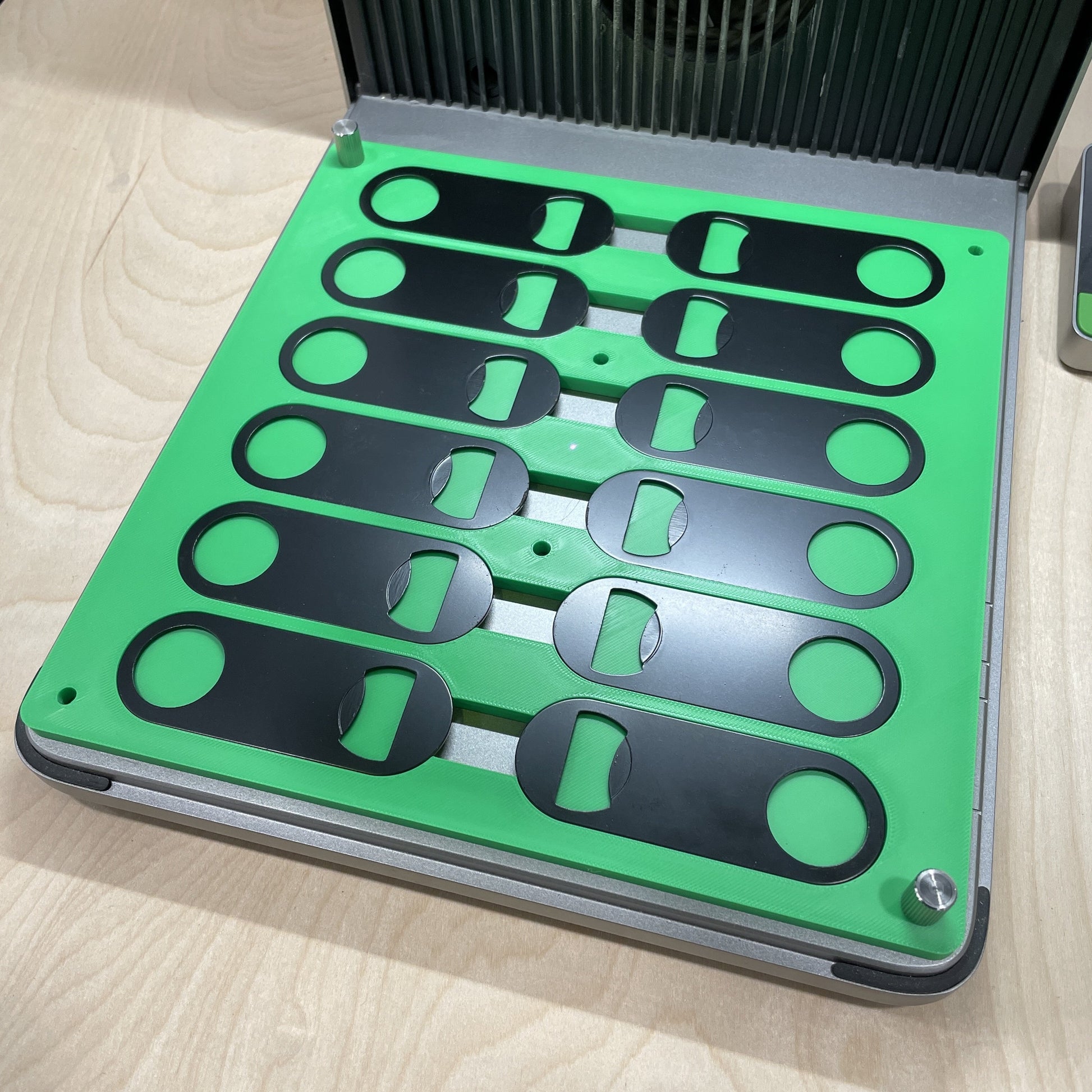 Empty Samcraft green flat oval keychain bottle opener jig in an xTool F1 Ultra laser bed, showing rows of shaped recesses.