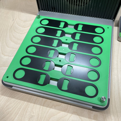 Empty Samcraft green flat oval keychain bottle opener jig in an xTool F1 Ultra laser bed, showing rows of shaped recesses.