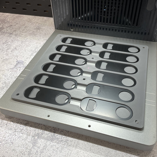 Empty Samcraft flat oval keychain bottle opener jig on the xTool F2 Ultra bed, showing rows of shaped recesses.