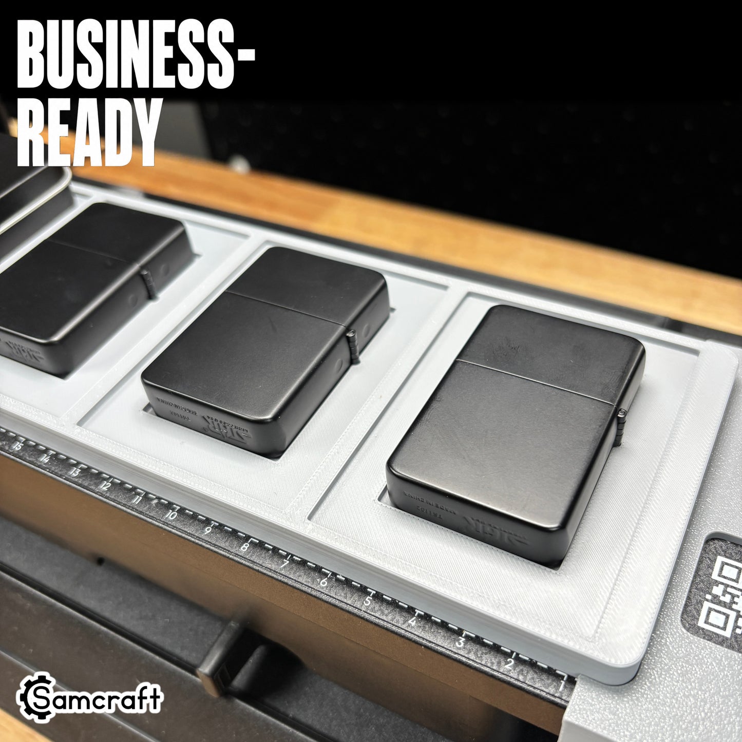Close-up of matte black flip-top lighters seated in the Samcraft jig's recessed pockets, demonstrating business-ready output and the built-in alignment ruler on the eufyMake E1.