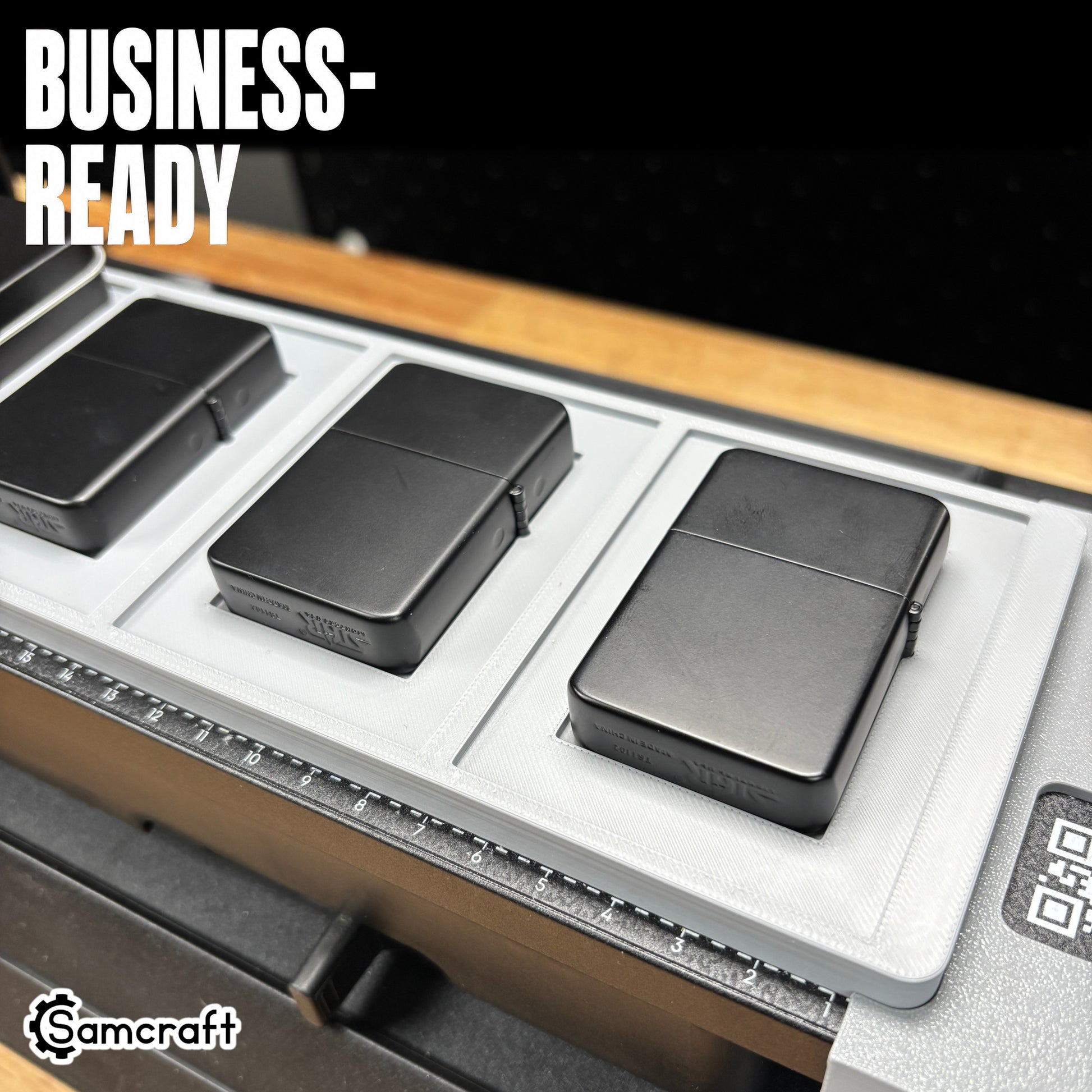 Close-up of matte black flip-top lighters seated in the Samcraft jig's recessed pockets, demonstrating business-ready output and the built-in alignment ruler on the eufyMake E1.