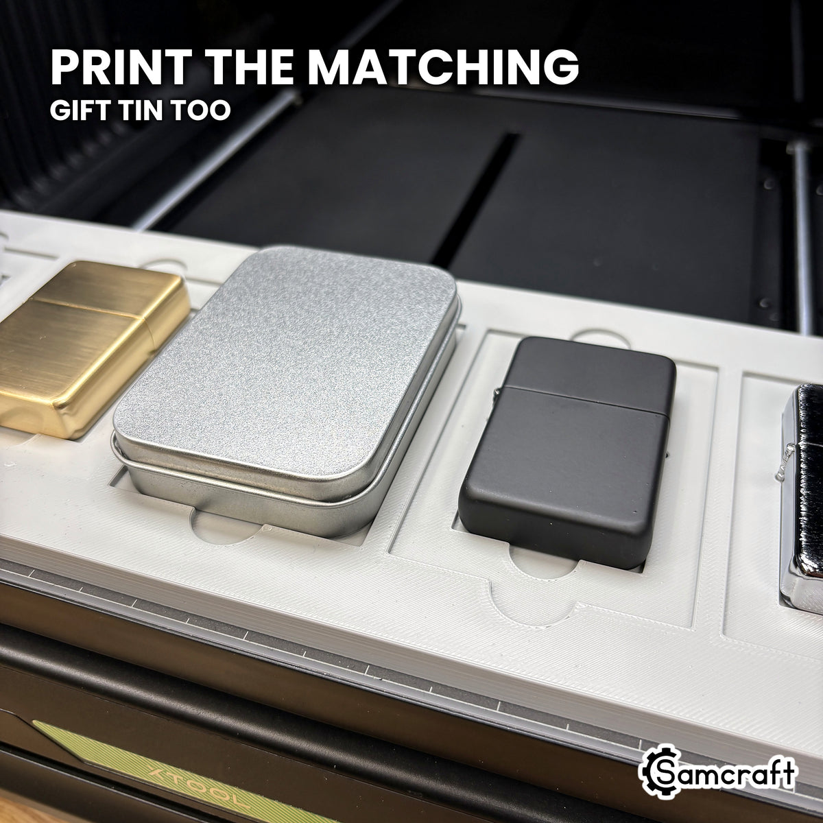 A gift tin case seated beside flip top lighters in the Samcraft xTool Omni jig, so a lighter and its tin can be printed as a matching set.