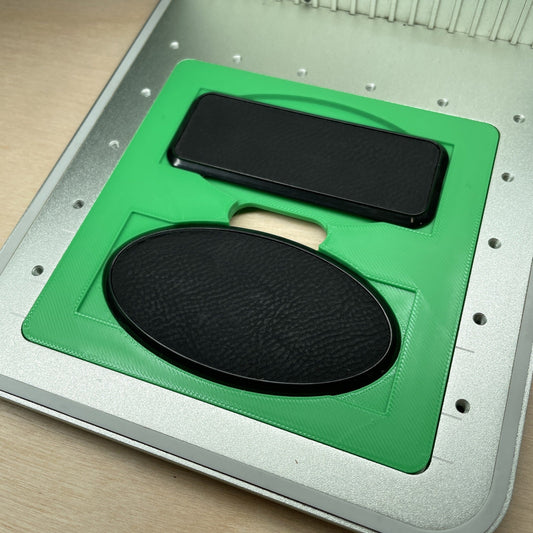 Samcraft framed badge jig in an xTool F1 laser bed, holding a black rectangular badge above a black oval badge.