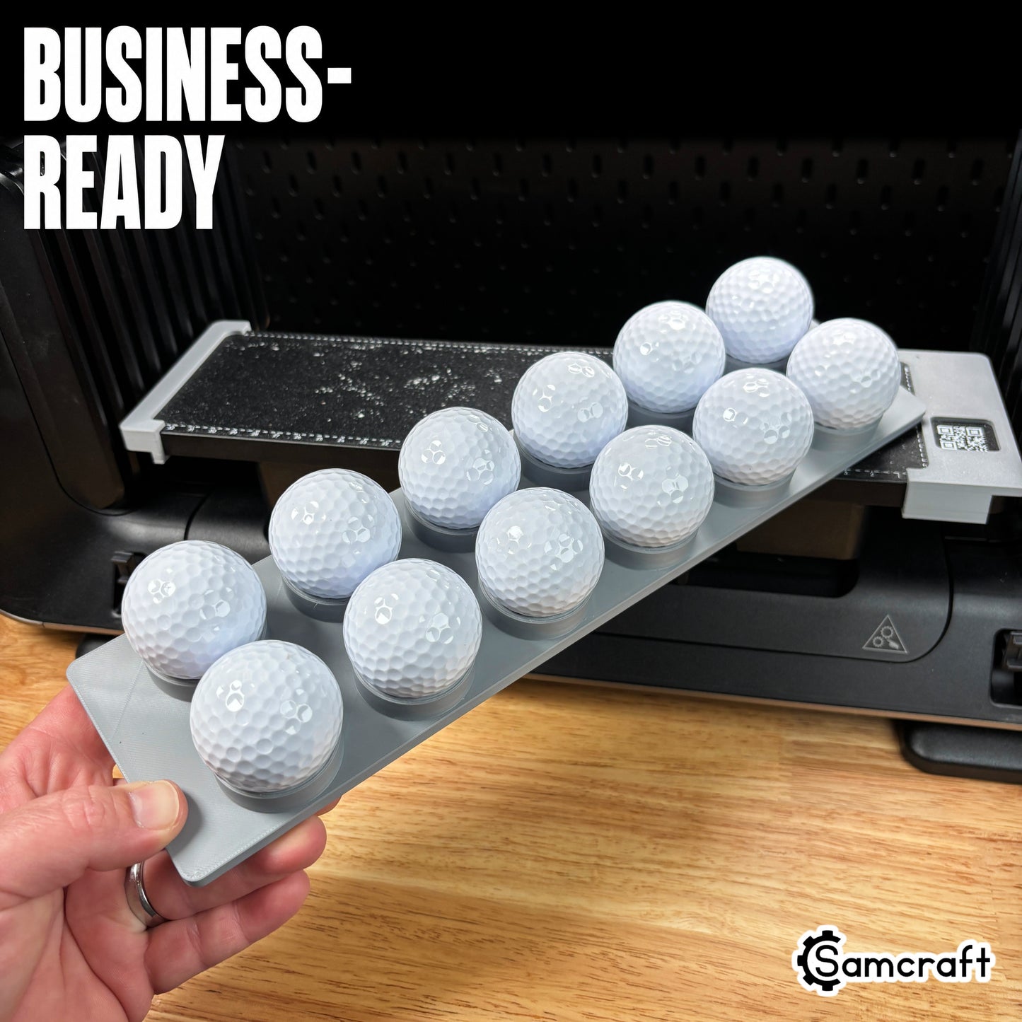 Hand holding the Samcraft Golf Ball Jig loaded with white golf balls in recessed cradles, ready for business production on the eufyMake E1 UV printer.