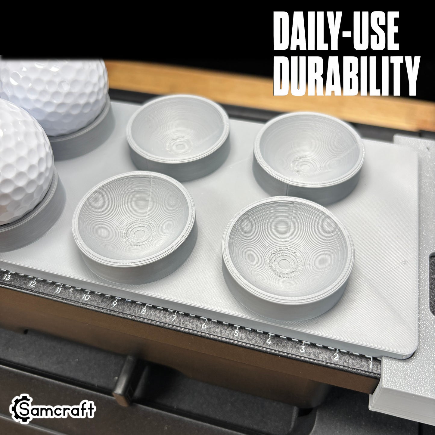 Close-up of the Samcraft Golf Ball Jig's round recessed cradles in a durable gray tray with white golf balls and built-in alignment ruler on the eufyMake E1.