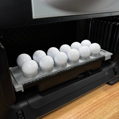 Samcraft golf ball jig on the bed of a eufyMake E1 UV printer, cradling eleven white golf balls in stepped ring holders.