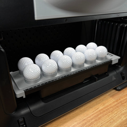 Samcraft golf ball jig on the bed of a eufyMake E1 UV printer, cradling eleven white golf balls in stepped ring holders.