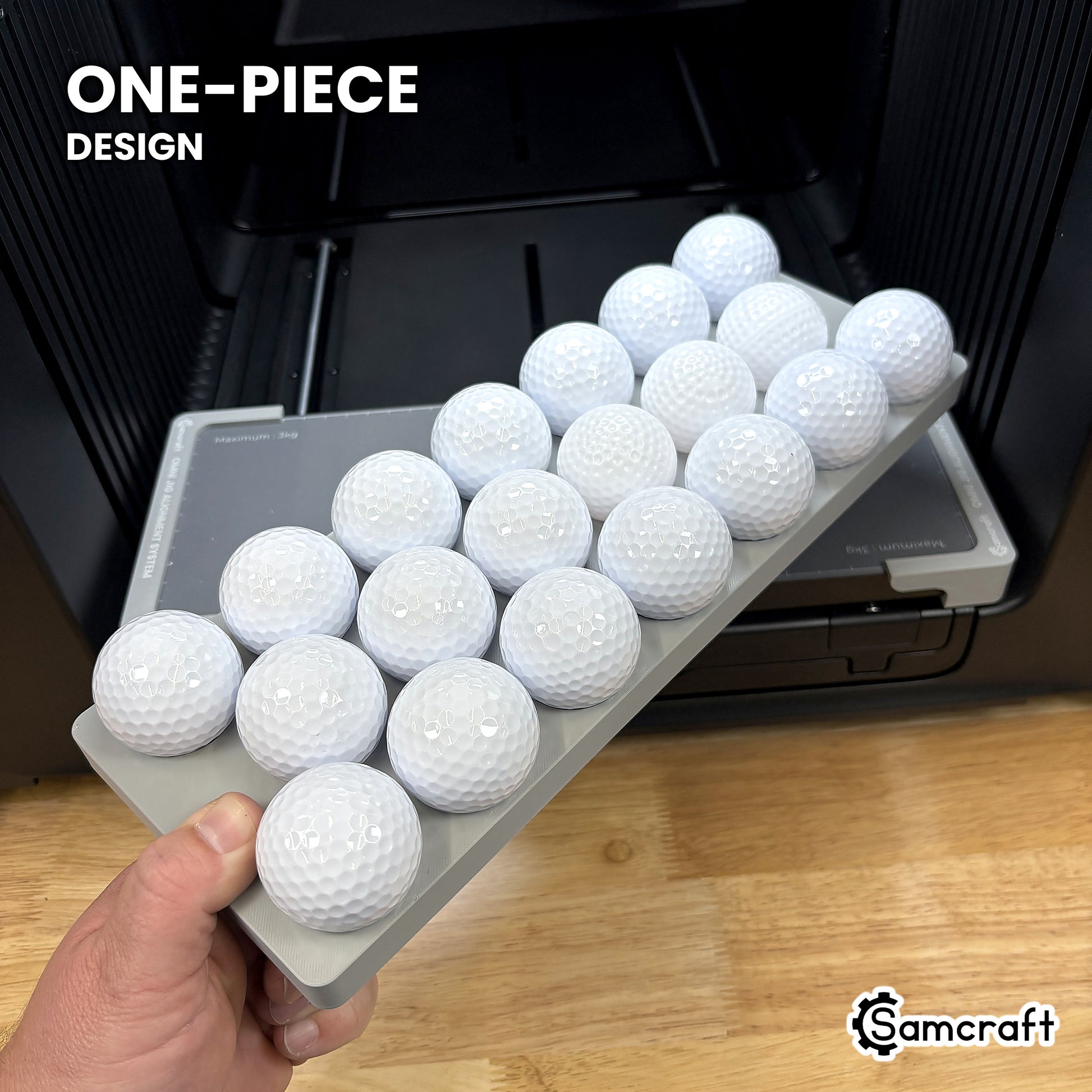 Hand holding the one-piece Samcraft golf ball jig for the xTool Omni, loaded with twenty white golf balls in a single molded gray tray.