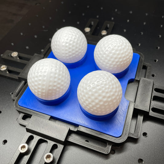 Samcraft blue golf ball and table tennis ball jig on a ComMarker laser bed, cradling four white golf balls.