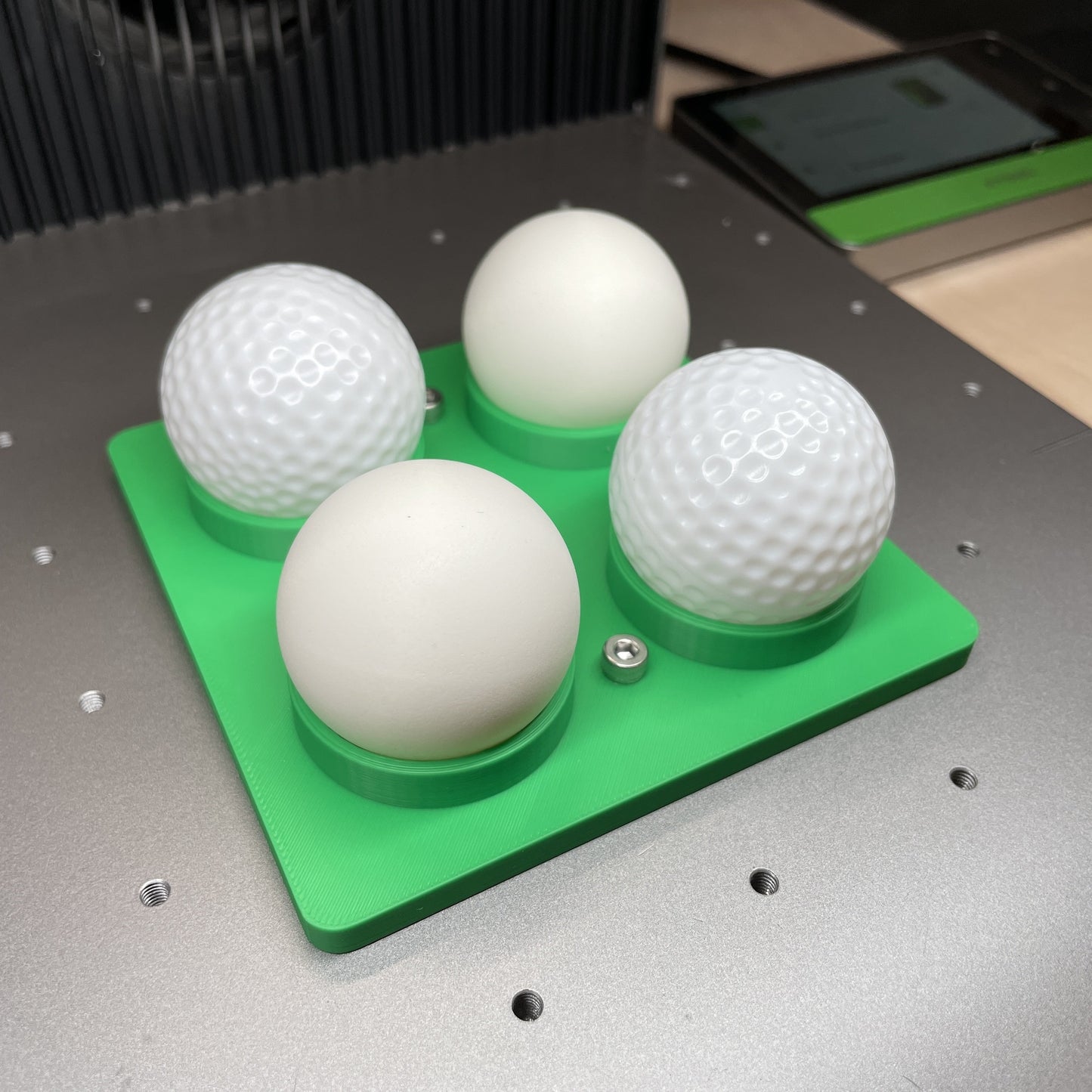 Samcraft green golf ball and table tennis ball jig in an xTool F1 Ultra laser bed, cradling four white balls.