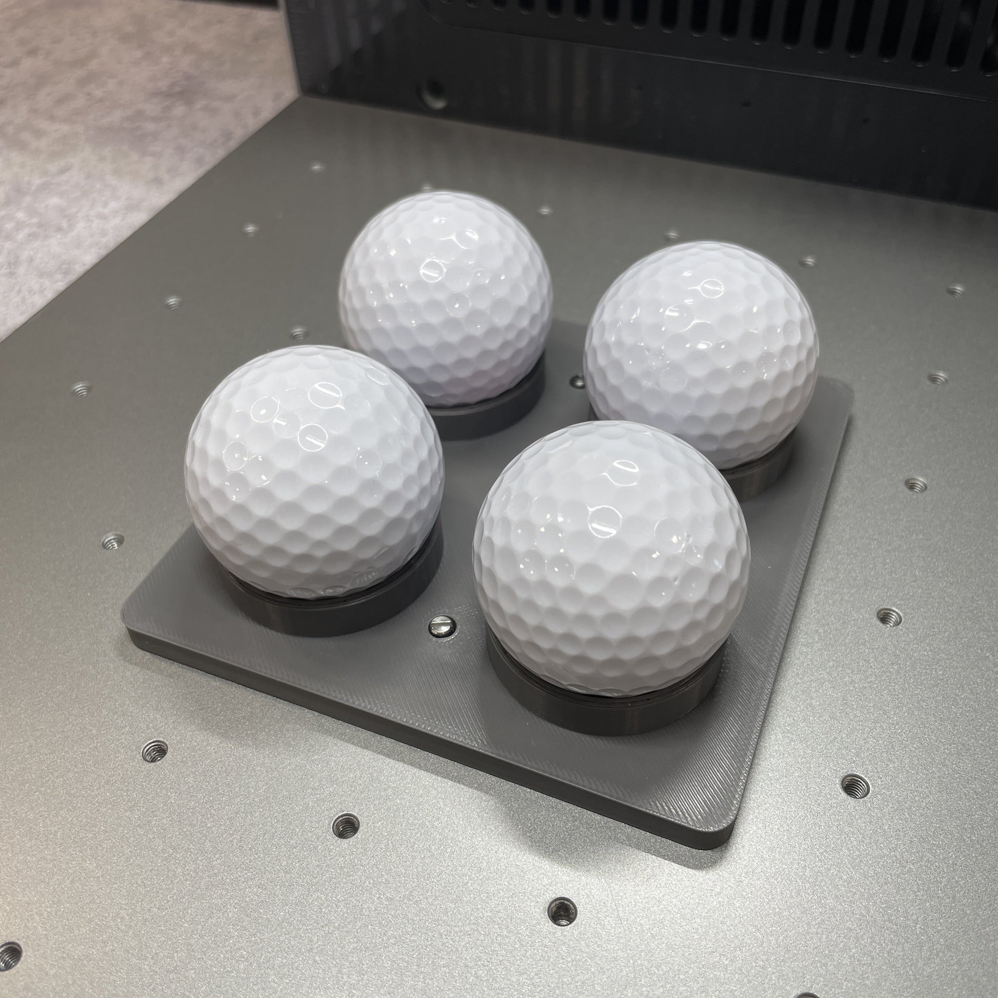 Samcraft golf ball and table tennis ball jig on the xTool F2 Ultra bed, cradling four white golf balls.