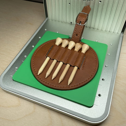 Samcraft golf tee and holder jig in an xTool F1 laser bed, holding a round tan leather golf tee holder loaded with five wooden tees.