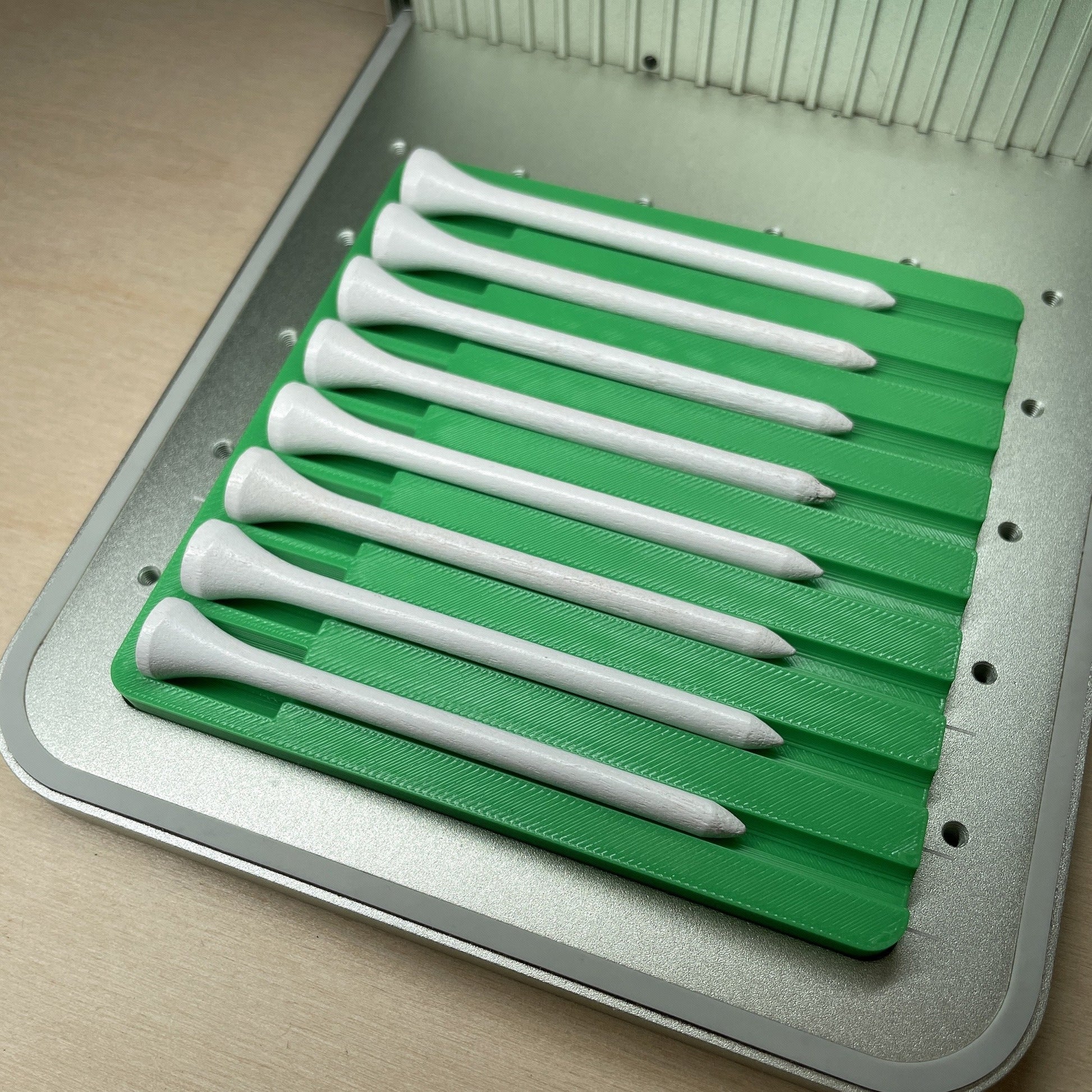 Samcraft golf tee jig in an xTool F1 laser bed, holding eight white golf tees angled across the jig.