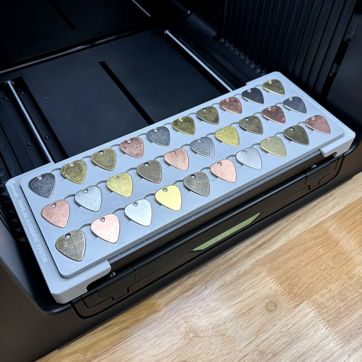 Samcraft guitar pick jig on the bed of an xTool Omni UV printer, loaded with a full tray of picks.