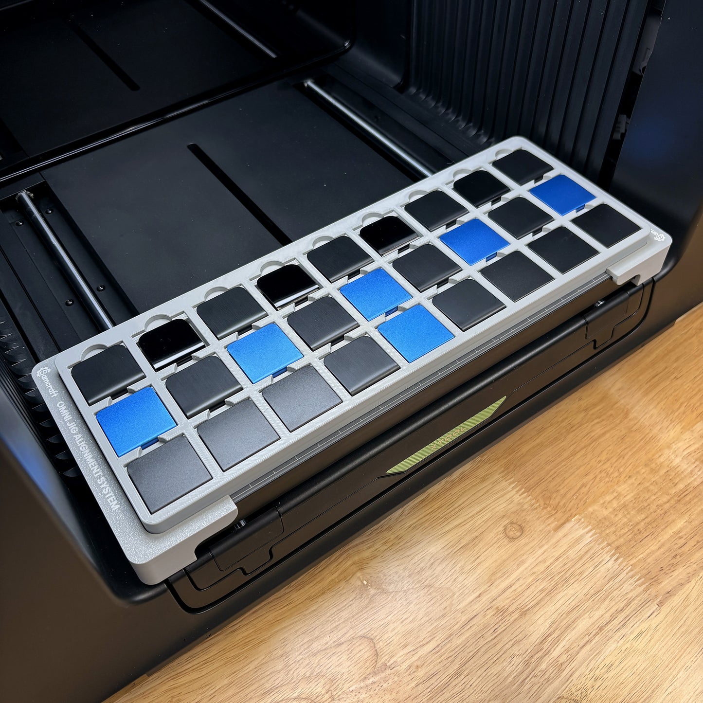 Samcraft hat brim clip jig on the bed of an xTool Omni UV printer, holding twenty-seven clips in blue and black.