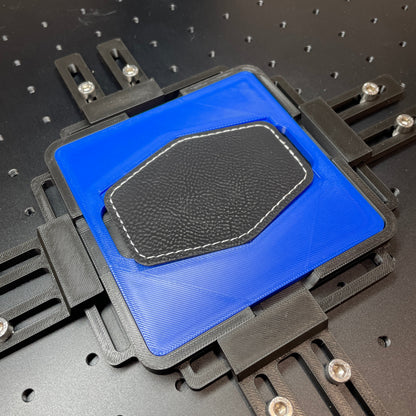 Samcraft blue hex patch jig on a ComMarker laser bed, holding a black hexagonal leatherette patch.